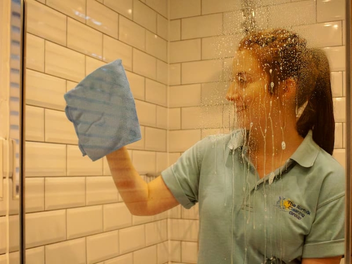 A woman diligently cleaning a shower using a blue cloth as part of the cleaning services provided by Norfolk Cleaning, ensuring a spotless and hygienic environment.